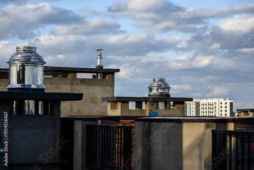 Rooftop ventilation systems with metal chimneys against cloudy sky