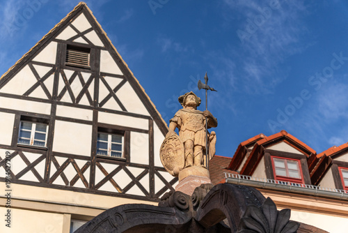 Landscape view of the statue on the Staupen Fountain (Market Fountain) at the market square opposite the Old Town Hall in Merseburg, Germany, with historic half-timbered houses in the background.
