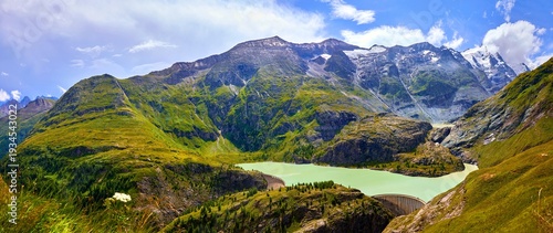Panoramic view at Pasterze Glacier Grossglockner Lake dam among austrian Alps mountains summits blue sky clouds.
