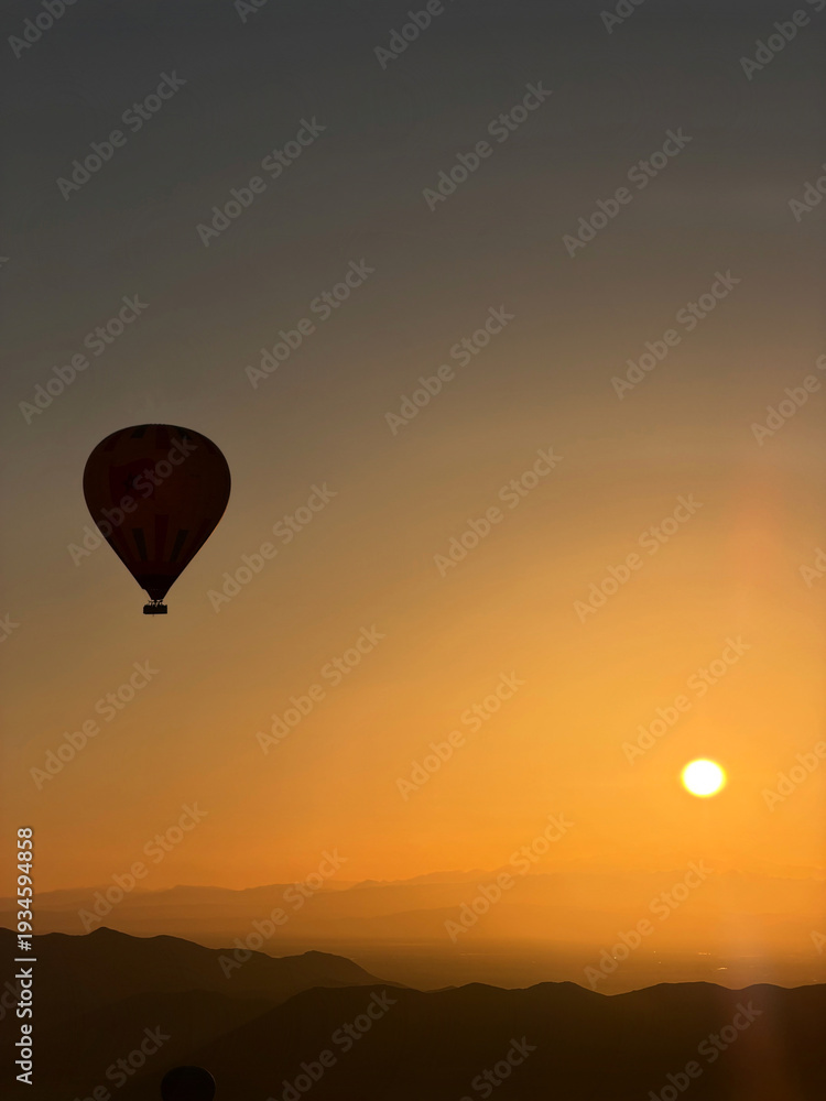 Naklejka premium Single Hot Air Balloon Silhouette a Vibrant Orange Sunrise Sky in Morocco