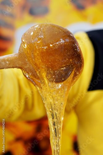 Close-up of golden organic honey dripping from a wooden spoon, highlighting its thick, sticky texture and vibrant amber color