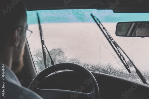 Driver operating vehicle while windshield wipers clear heavy rain during commute
