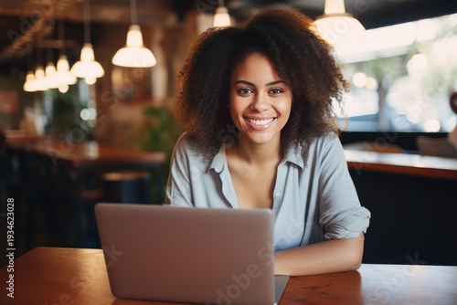 Free Download Young black woman smiling, looking at camera while working remotely on laptop in a cafe - GFXLoad