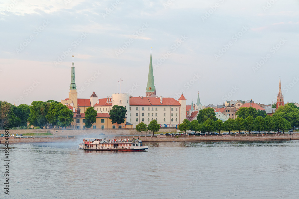 Obraz premium A pleasure boat sails along the Dune River in Riga, Latvia, with Riga Palace in the background The photo was taken at dusk