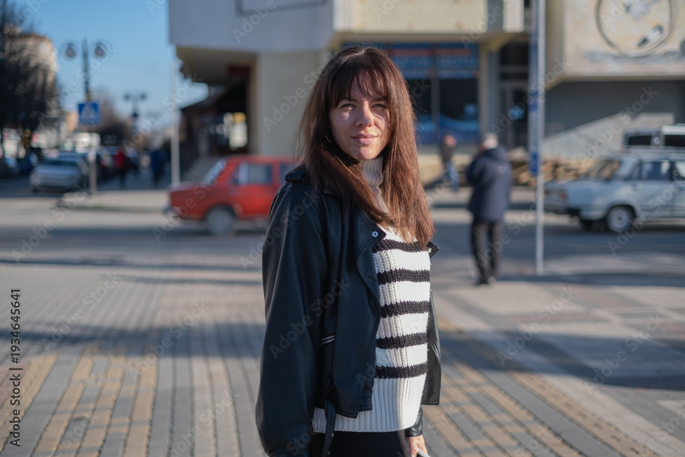 Obraz premium Young woman stands on a city street enjoying a day of exploration with people and cars around her during afternoon light