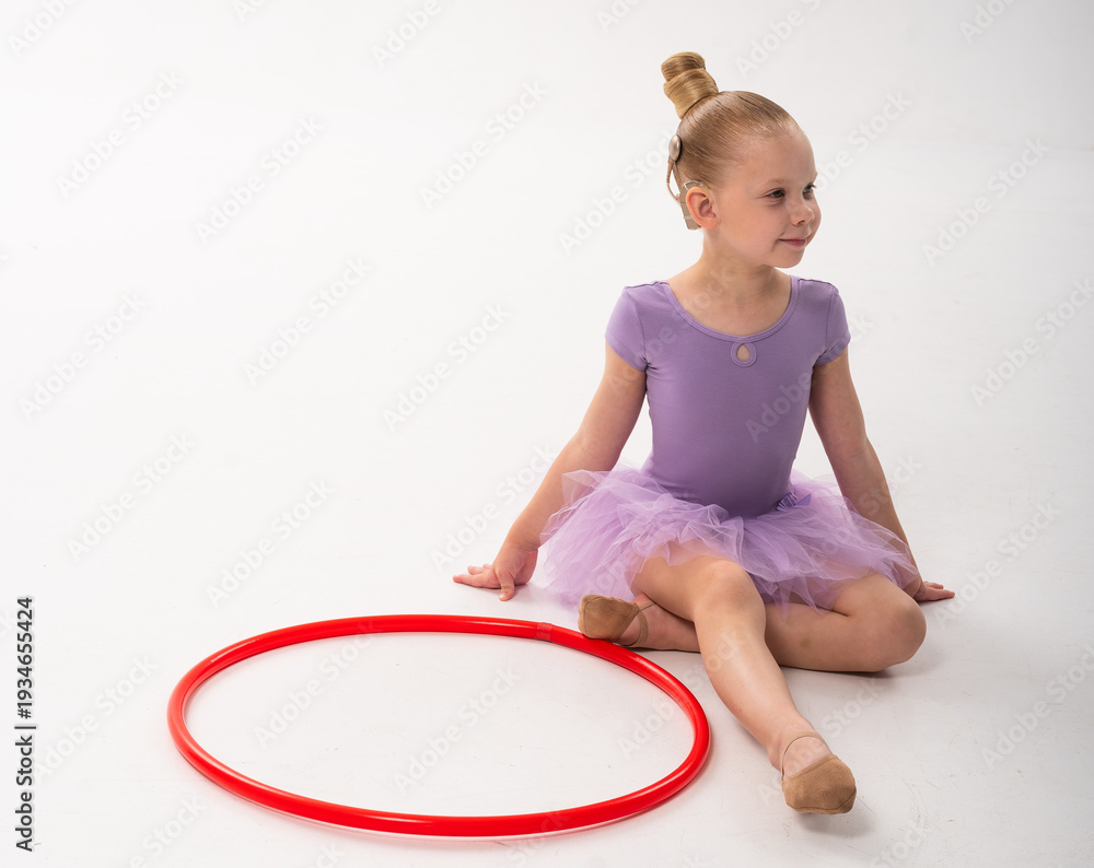 Obraz premium Child ballerina with cochlear implant sitting near red hoop. Inclusive beauty, hearing technology, and self-confidence expressed through dance and childhood joy.