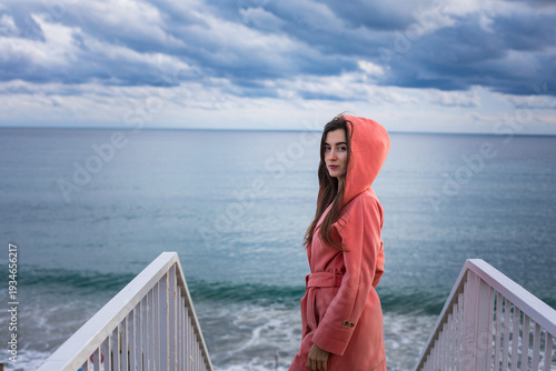 a girl in a coral coat against the backdrop of the sea in autumn