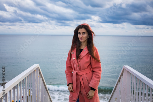 a girl in a coral coat against the backdrop of the sea in autumn