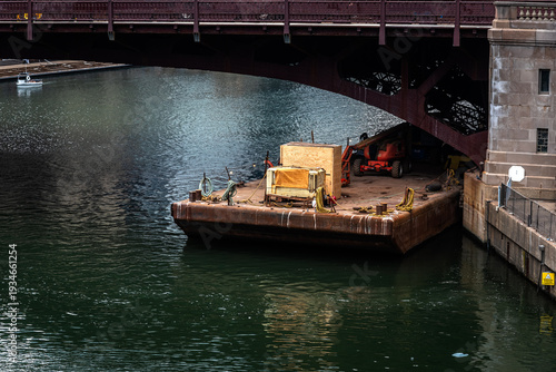 Barge carrying construction equipment under a bridge on the Chicago River in downtown Chicago.