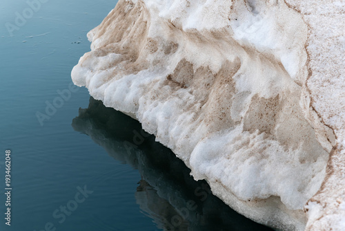 Chunk of ice hangs over the surface of the lake and is reflected in it.