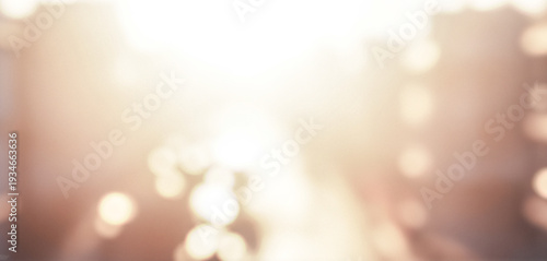 Blurred cityscape with bright sunlight creating a soft glow. Urban environment features indistinct buildings and warm bokeh effects with luminous highlights.