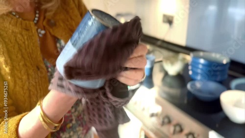 close up of middle aged woman cleaning blue mug with black tea towel in kitchen
