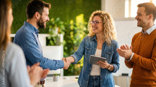 Business colleagues shaking hands in modern office with green wall, celebrating success and teamwork achievement among diverse group of professionals