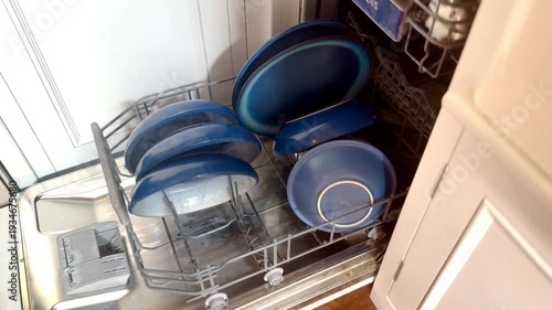 woman emptying blue crockery bowls from modern kitchen dishwasher