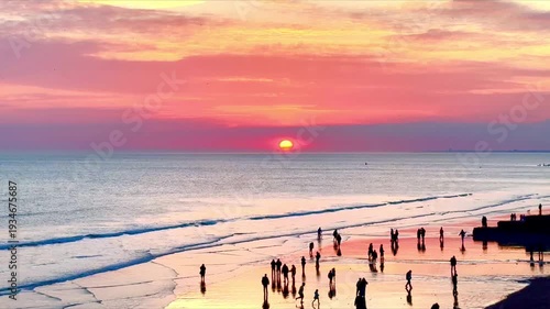 beautiful colorful sunset sky over water with silhouettes of people on beach 