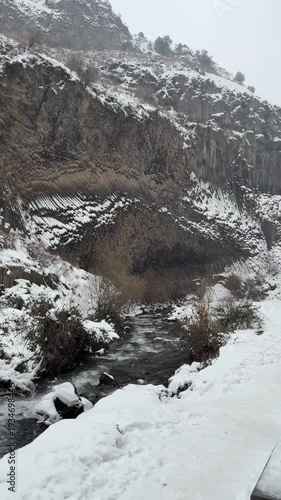 Snow-covered basalt columns of Symphony of Stones in Garni Gorge, Armenia, with river flowing through winter canyon landscape. Dramatic natural rock formation, cold season travel destination