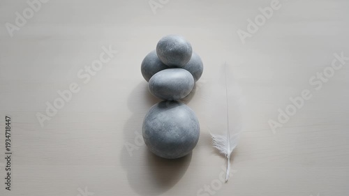 Stacked gray stones and a white feather rest on a light wooden surface