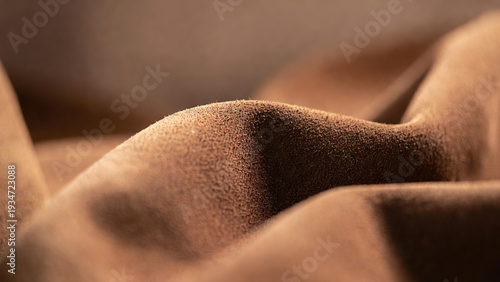 Extreme close up of textured brown suede fabric showing fine fibers and soft folds. High quality material background for fashion, upholstery, and leather goods industries.