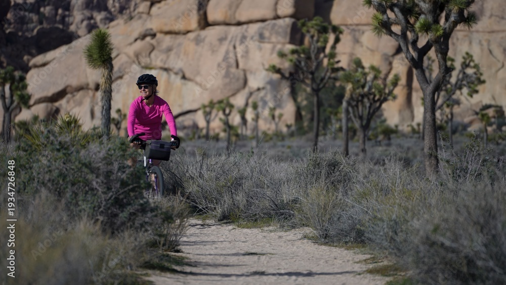 Fototapeta premium Mature woman bikes along dirt paths in Joshua Tree National Park in California while exploring the natural beauty of the area