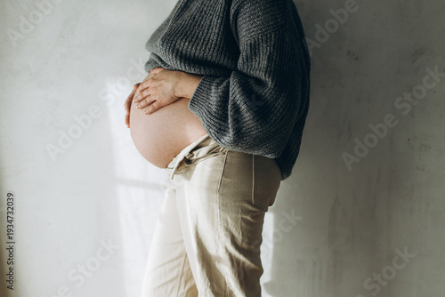 Stylish pregnant woman hugging baby bump close up. Happy Mothers day! Healthy pregnancy and fertility concept. Happy woman in cozy sweater and jeans holding pregnant belly