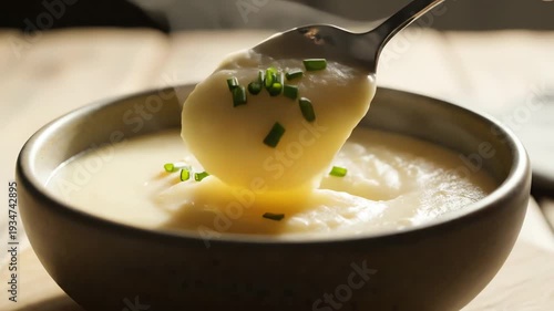 Creamy soup in a dark bowl with a spoon and fresh herbs