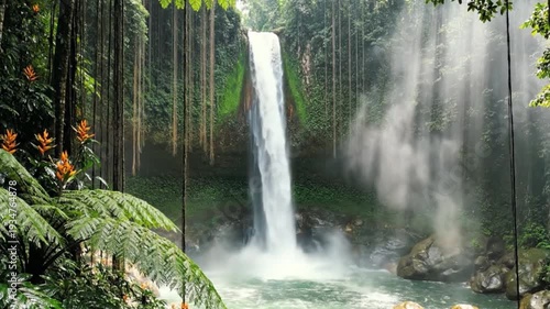 A stunning waterfall cascades into a misty pool, framed by lush green vegetation and colorful flora