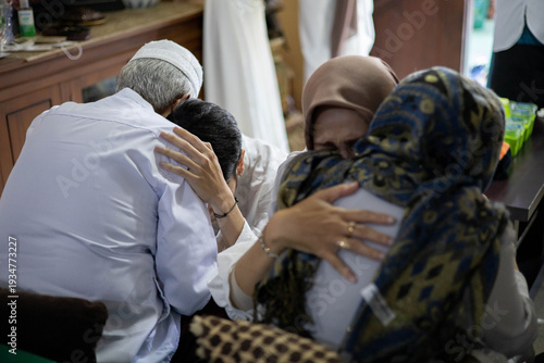 A poignant and emotional scene of an Indonesian Muslim family during Eid al-Fitr, showing a son and daughter-in-law deeply embracing their elderly parents while seeking forgiveness (Sungkem).
