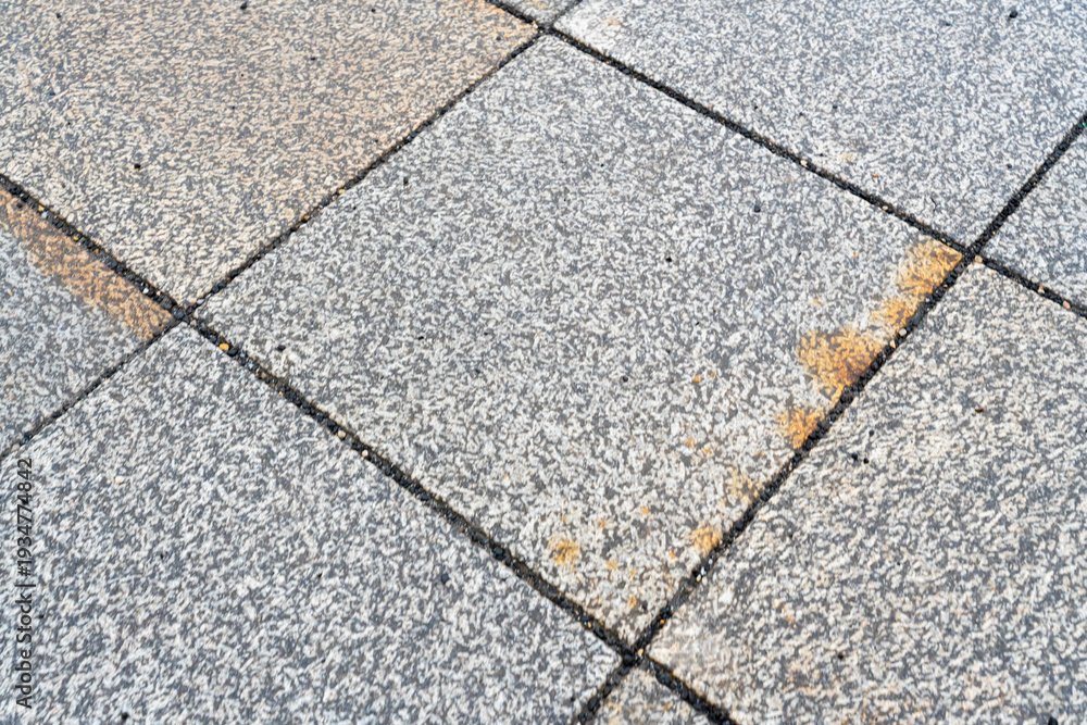 Obraz premium Close-up view of a textured gray stone pavement with visible dirt marks and light orange stains, showcasing urban infrastructure and surface wear, ideal for backgrounds in design.