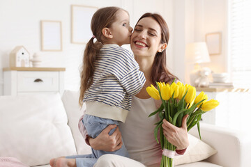 Happy Mother's Day. Little girl and her mom with beautiful tulips on sofa indoors