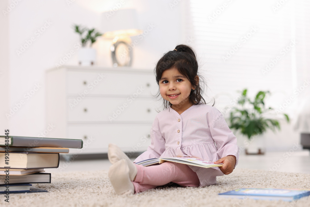 Naklejka premium Cute little girl reading book on floor at home. Space for text
