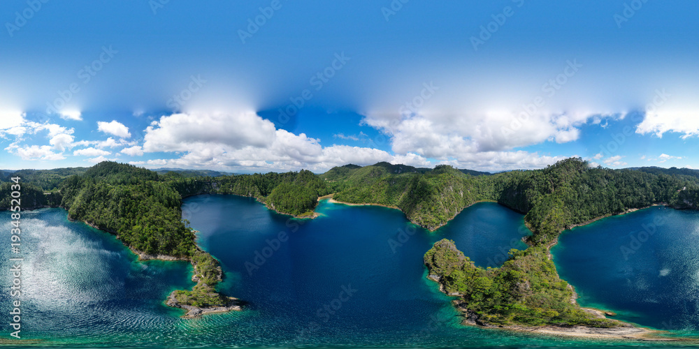 Fototapeta premium Aerial view of a turquoise lagoon surrounded by dense tropical vegetation. The irregular shape of the water forms small coves and tree-covered peninsulas, creating a striking contrast between the deep