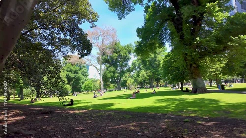 People relaxing on open lawns in Treasury Gardens, Melbourne, Australia. Inner-city public green space used for leisure, social gathering, and recreation within a historic urban park.