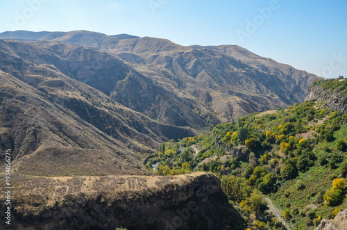 Rolling hills under a blue sky. Green trees frame the foreground, overlooking a vast, arid valley. Armenia