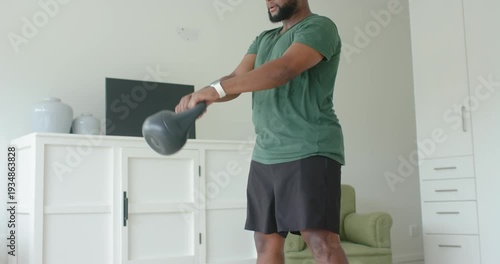 African American man spotting kettlebell on floor performing swings in living room for fitness