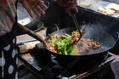 Foto Street vendor cooking thai stir fry in hot wok with fresh basil and ingredients