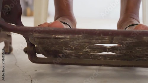 Closeup toes pressing black treadle pedal on house floor, sandal shifting on metal grate, deliberate press and release motion, close rhythm for mending or tailoring, intimate workshop to home vibe