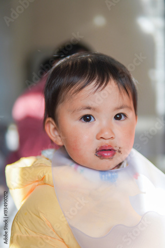 Adorable toddler girl with chocolate stains on her mouth looking at camera. Messy eating, childhood innocence, and sweet snacks concept.