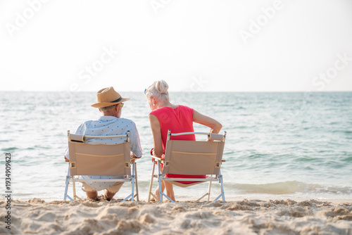 Quadro su tela Happy senior couple sitting on a chair on the shore of the beach