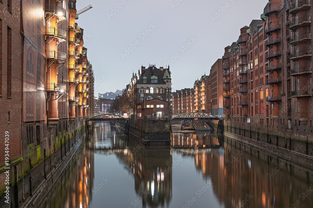 Fototapeta premium Experience the enchanting charm of Hamburg s Speicherstadt at twilight. Its historic warehouses and canal reflections showcase Hamburg s unique architectural beauty and allure.