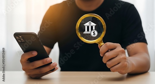 Person examining financial institution symbol with magnifying glass while holding smartphone in a well lit environment with a wooden table.