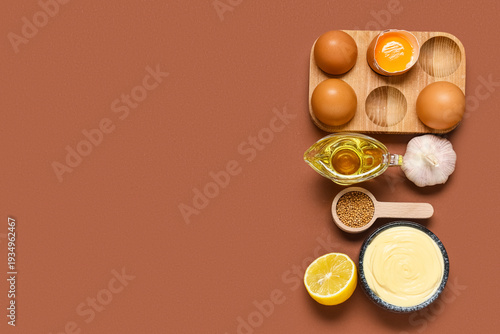 Bowl with tasty mayonnaise sauce and different ingredients on brown background