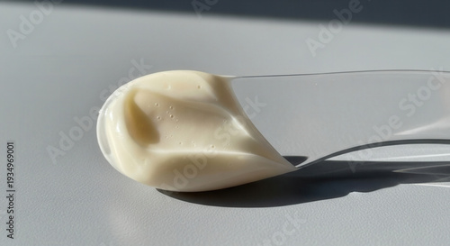 Close-up of a clear plastic beauty spatula with a rich dollop of ivory cosmetic cream, featuring a smooth texture and soft natural shadows.