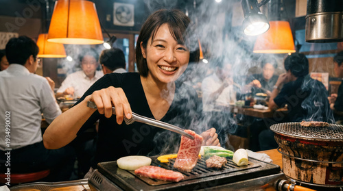煙が立ち上る鉄板で焼肉を焼くショートヘアの明るい女性