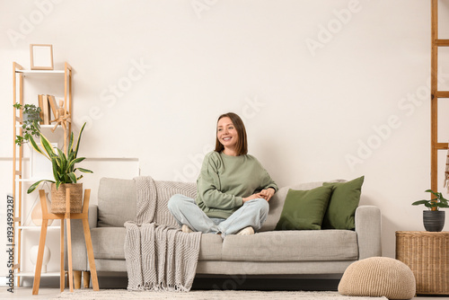 Happy young woman sitting on grey sofa in living room