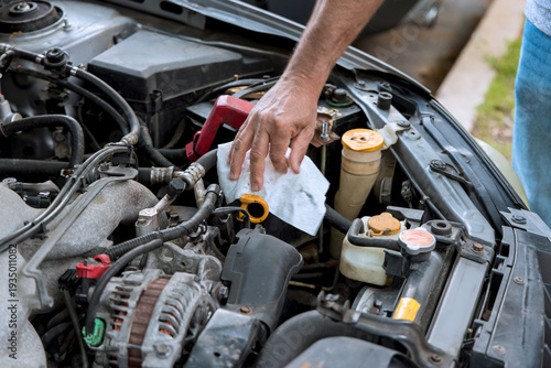 Worker inspects engine components wipes fluid caps while performing vehicle maintenance in service garage