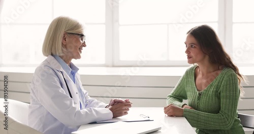 Female doctor in white coat sits at desk and explains medical results to woman patient, clarifying diagnosis, treatment options during consultation in clinic office. Professional health care services