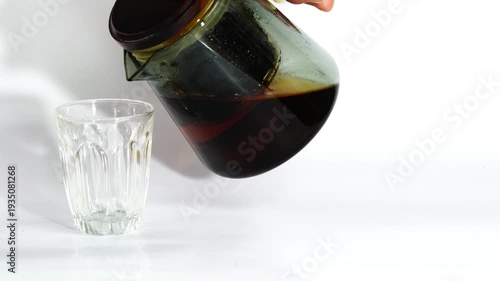 Pouring freshly brewed hot tea fron glass teapot into a small teaglass on white background.