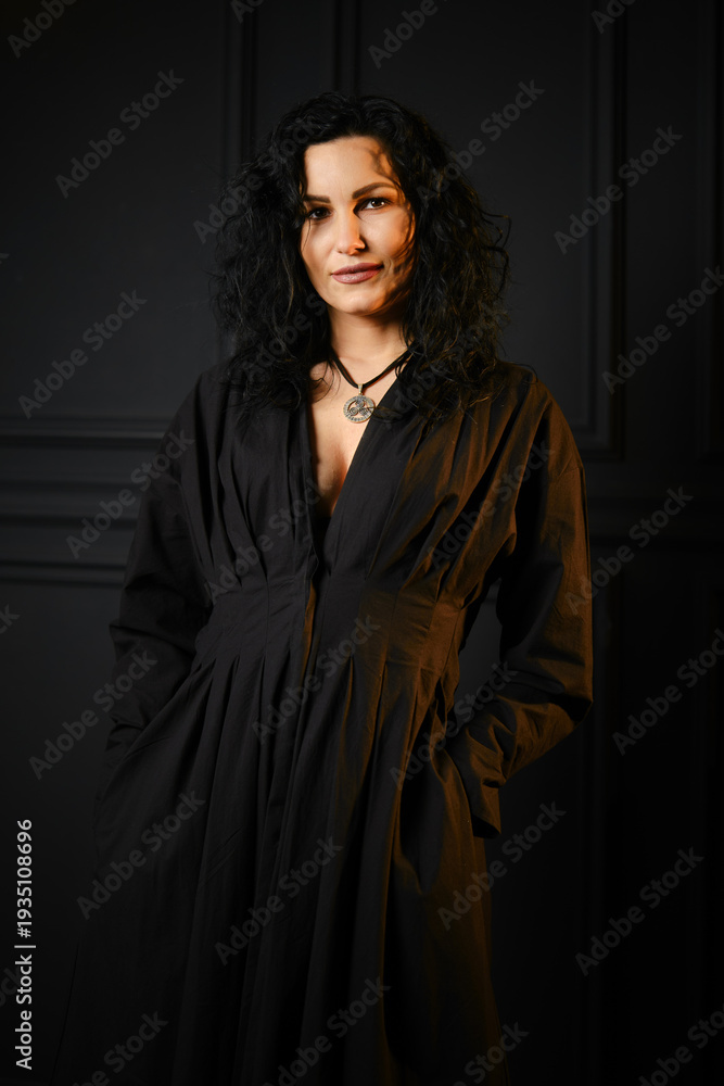 Naklejka premium Woman with dark hair stands indoors wearing a black outfit