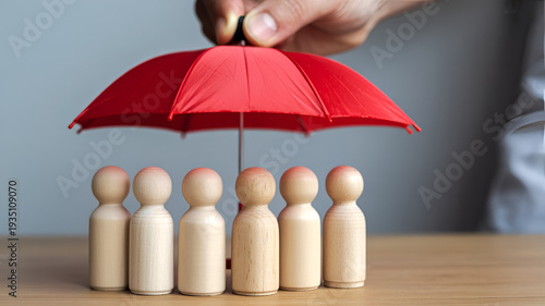 Hand holding red umbrella over six wooden figurines on wooden table protection concept insurance coverage safety security teamwork collaboration support care wooden people figurative representation