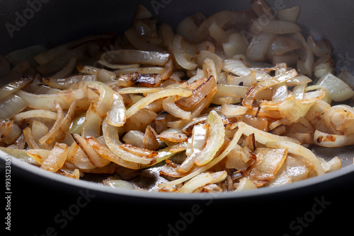 Sliced white onion frying in a deep ceramic frying pan background backdrop.